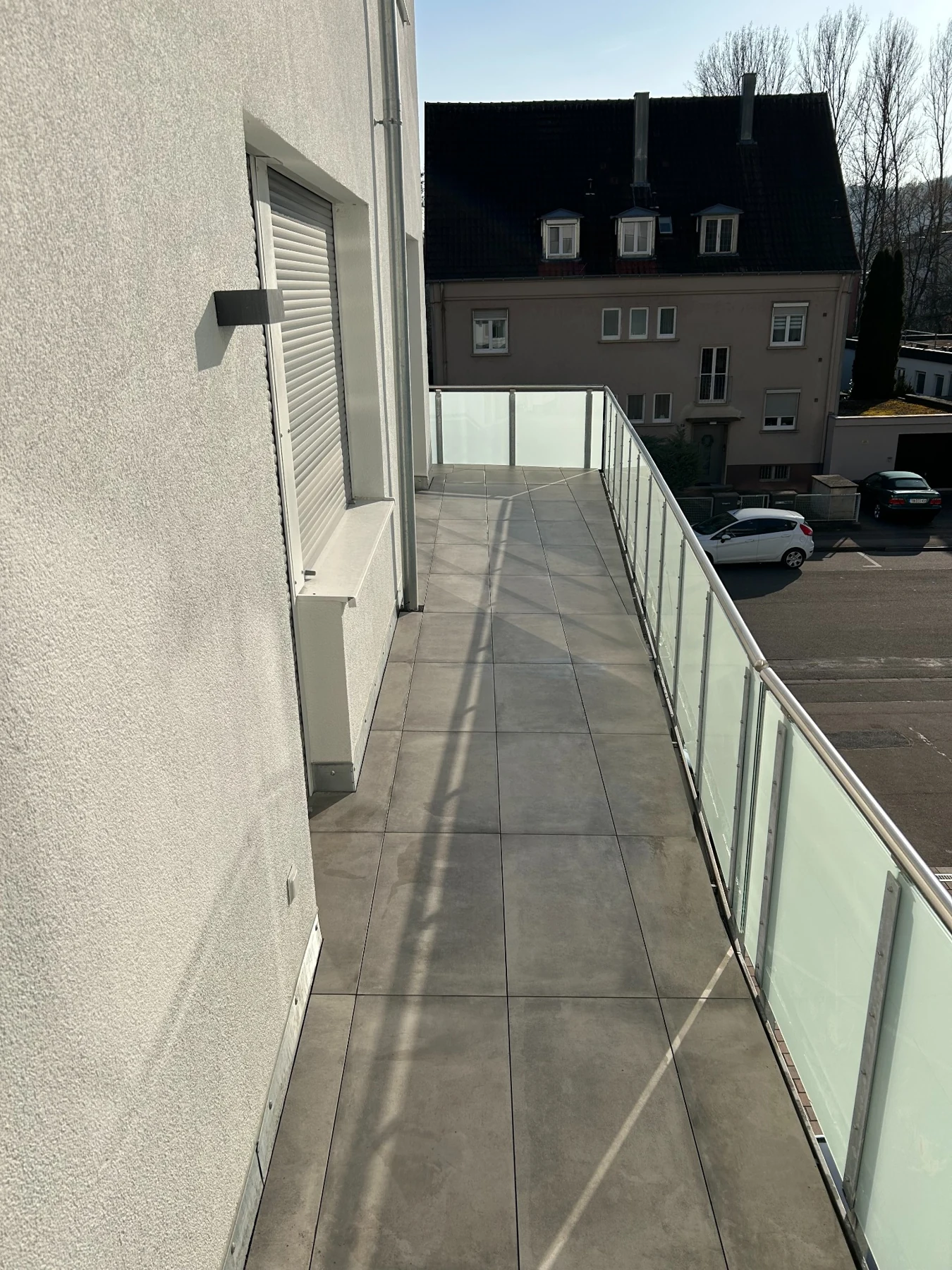 Langer Balkon mit Plattenbelag und Glasgeländer