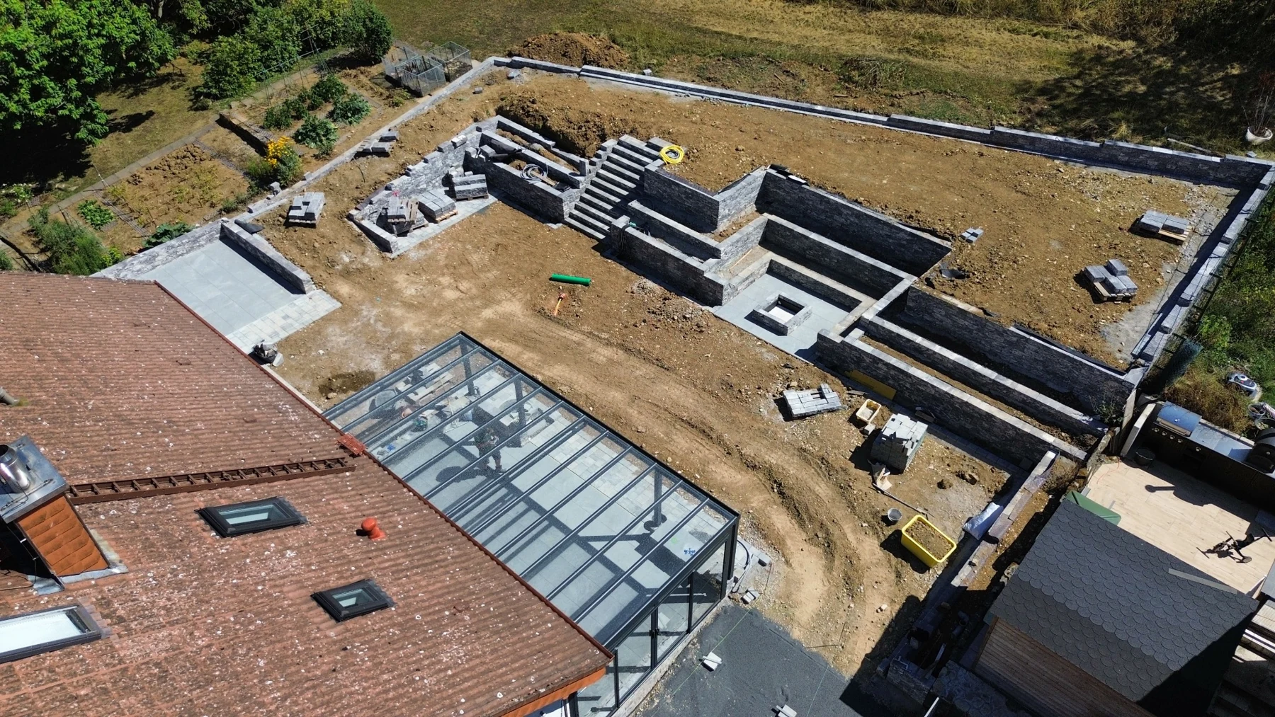 Drohnenansicht einer Außenanlage mit Natursteinmauern, Treppen und Terrassen während der Bauarbeiten